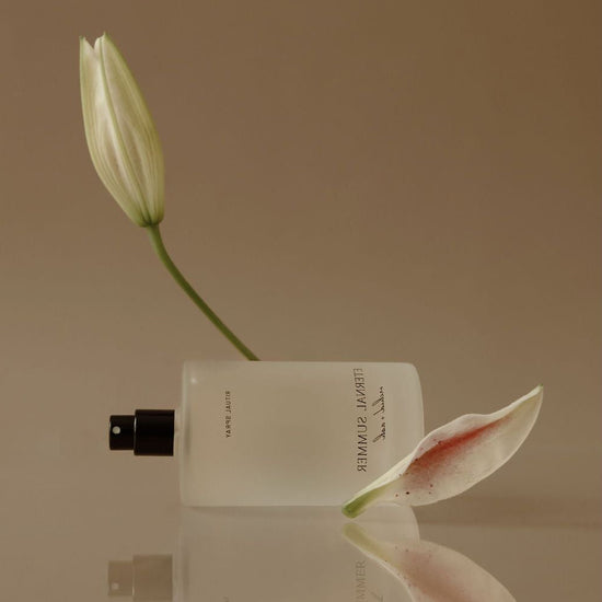 White flower bud and perfume bottle on a reflective surface with a beige background