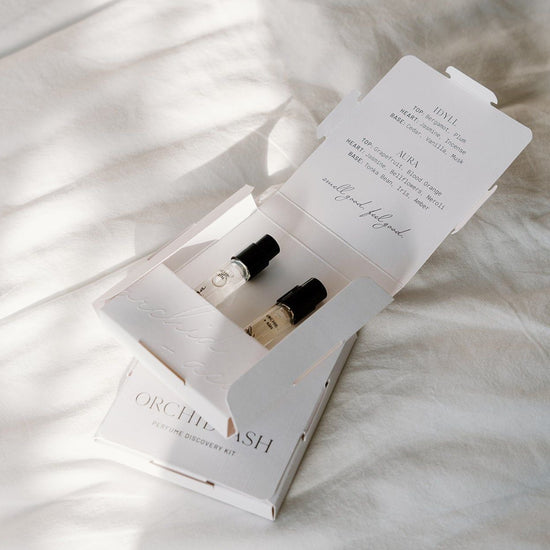 Two small bottles in an open box with a menu on a textured white surface