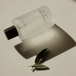 White bottle with black cap on a beige surface with a green leaf