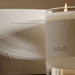 Candle with a glass container and a white box labeled 'ASL' on a reflective surface.