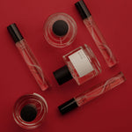 Five perfume bottles and roll-on bottles arranged on a solid red background. The set includes clear glass bottles with pink liquid, black caps, and one square bottle with a white label.
