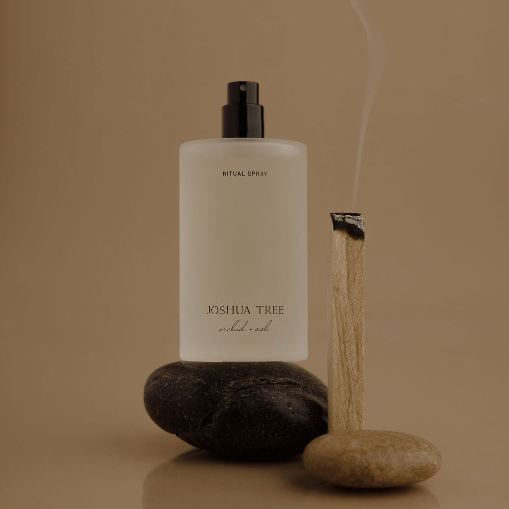 White bottle with black cap labeled 'Joshua Tree' on a reflective surface with stones and smoke on a beige background