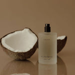 Coconut shell and bottle on a reflective surface with a beige background