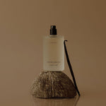 Moisturizing spray bottle on a coconut with a vanilla bean against a brown background