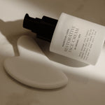 White face cream bottle with black cap on a marble surface