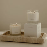 Two lit candles on a tray with a box labeled 'The White Company' against a neutral background.