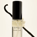Perfume bottle labeled 'IDYLL Orchid + Ash' with a black cap on a light background