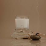 Candle with a label on a piece of driftwood against a beige background