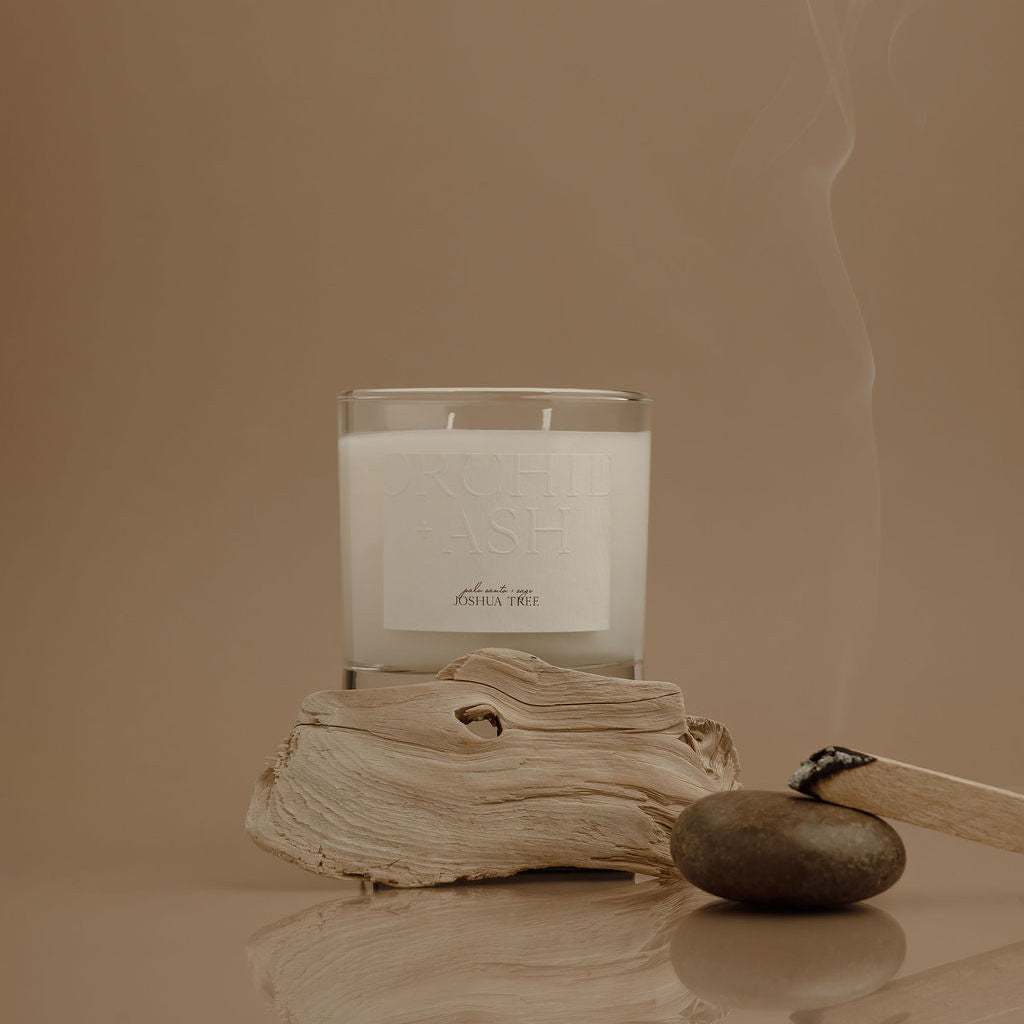 Candle with a label on a piece of driftwood against a beige background