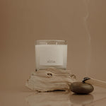 Candle with a label on a piece of driftwood against a beige background