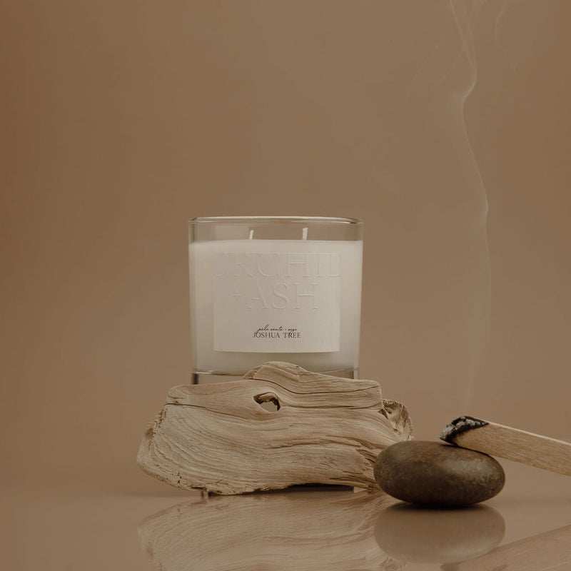 Candle with a label on a piece of driftwood against a beige background