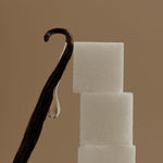 Vanilla bean next to three sugar cubes on a brown background