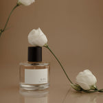 Perfume bottle with white flowers on a reflective surface and brown background