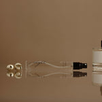 Two perfume bottles and a small container on a reflective surface with a beige background
