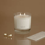 Candle with two lit flames on a reflective surface against a brown background