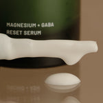 Serum bottle labeled 'Magnesium + GABA Reset Serum' on a reflective surface.
