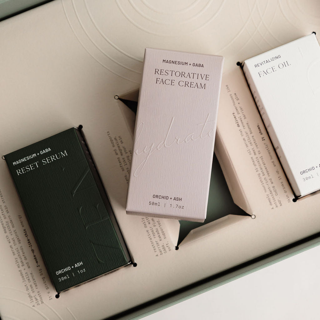 Skincare products including a black serum, purple cream, and white box on a light background.