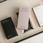 Skincare products including a black serum, purple cream, and white box on a light background.