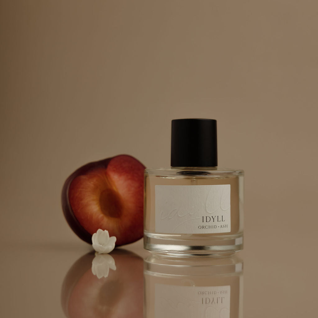 Perfume bottle labeled 'IDYLL' with a peach and white flower on a reflective surface.