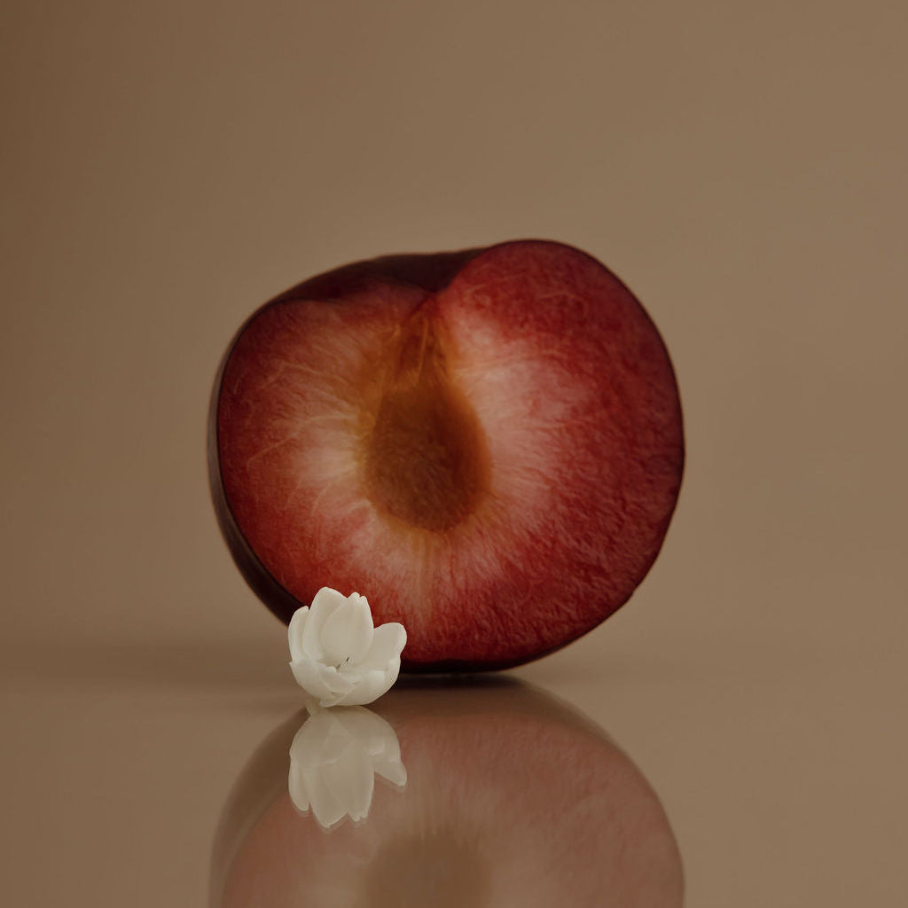 Halved plum with a white flower on a reflective surface against a brown background