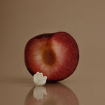 Halved plum with a white flower on a reflective surface against a brown background
