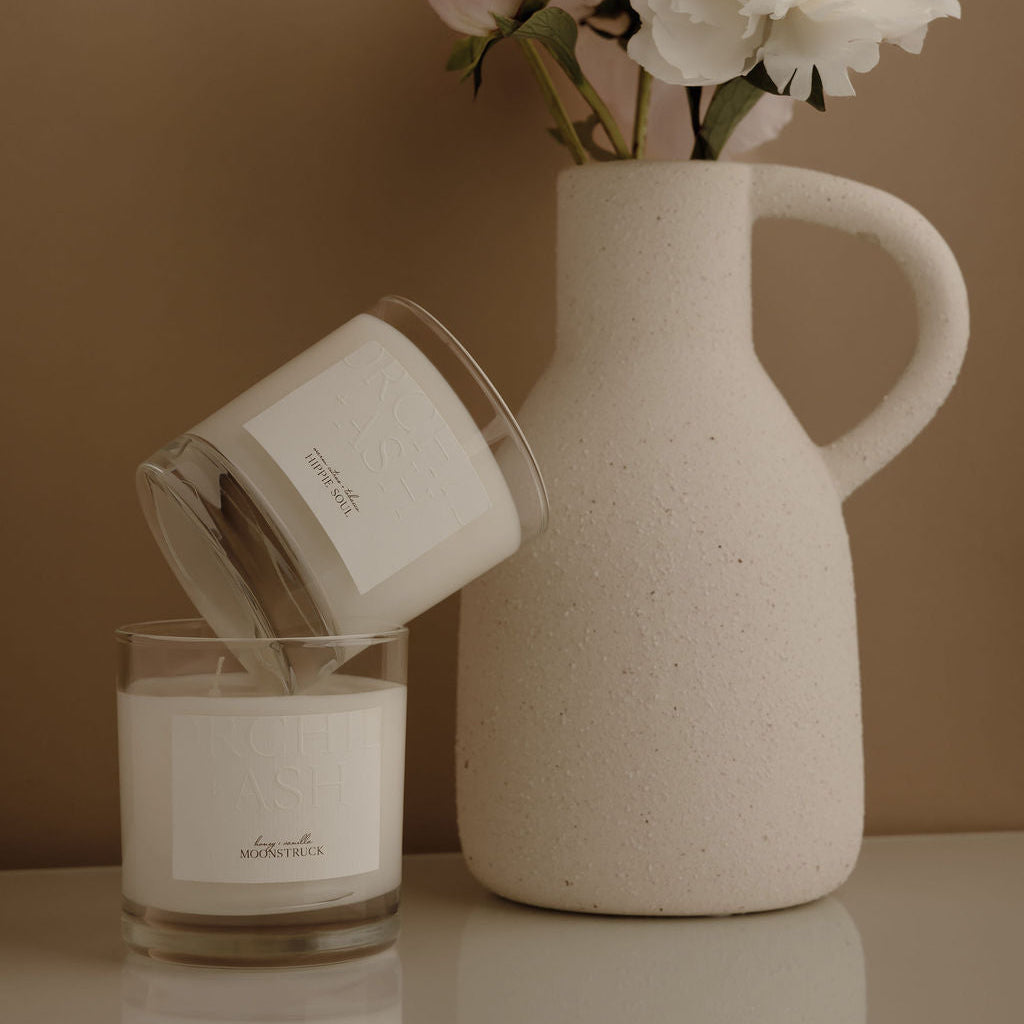 White candle and ceramic vase with flowers on a reflective surface against a brown background