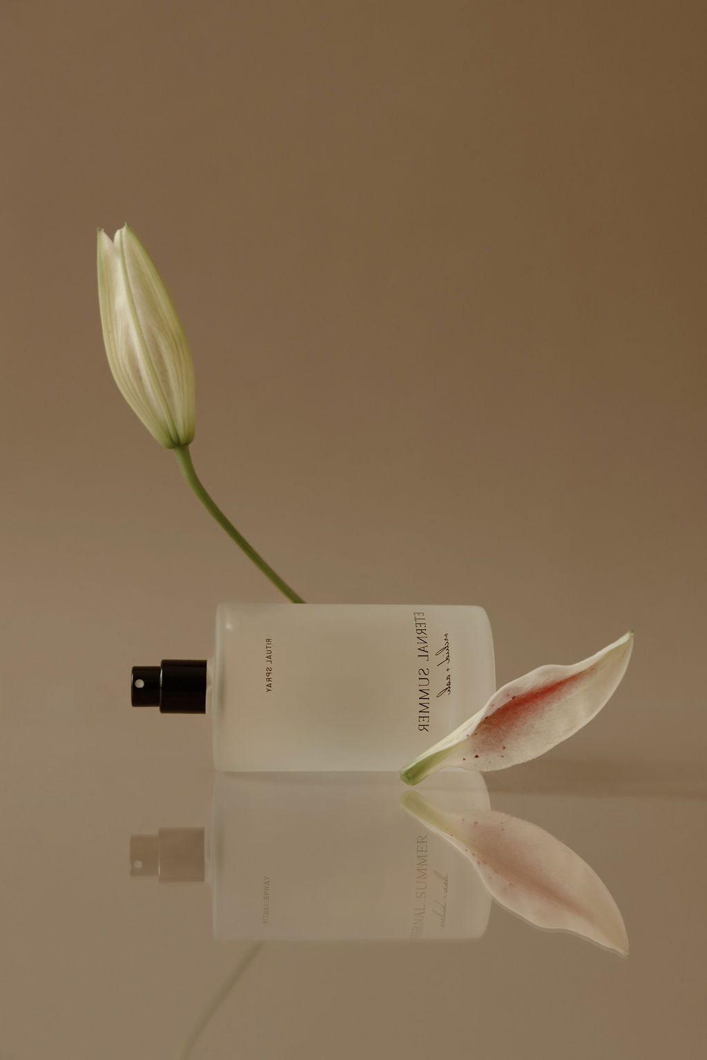 White flower bud and perfume bottle on a reflective surface with a beige background