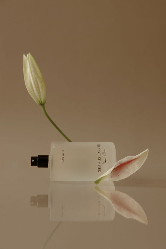White flower bud and perfume bottle on a reflective surface with a beige background