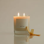 Lit candle in a glass jar with a label on a reflective surface