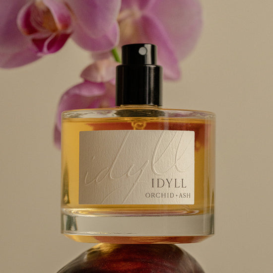 IDYLL Orchid & Ash perfume bottle with pink orchids in the background