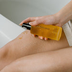Person applying a yellow bottle of body oil to their leg.