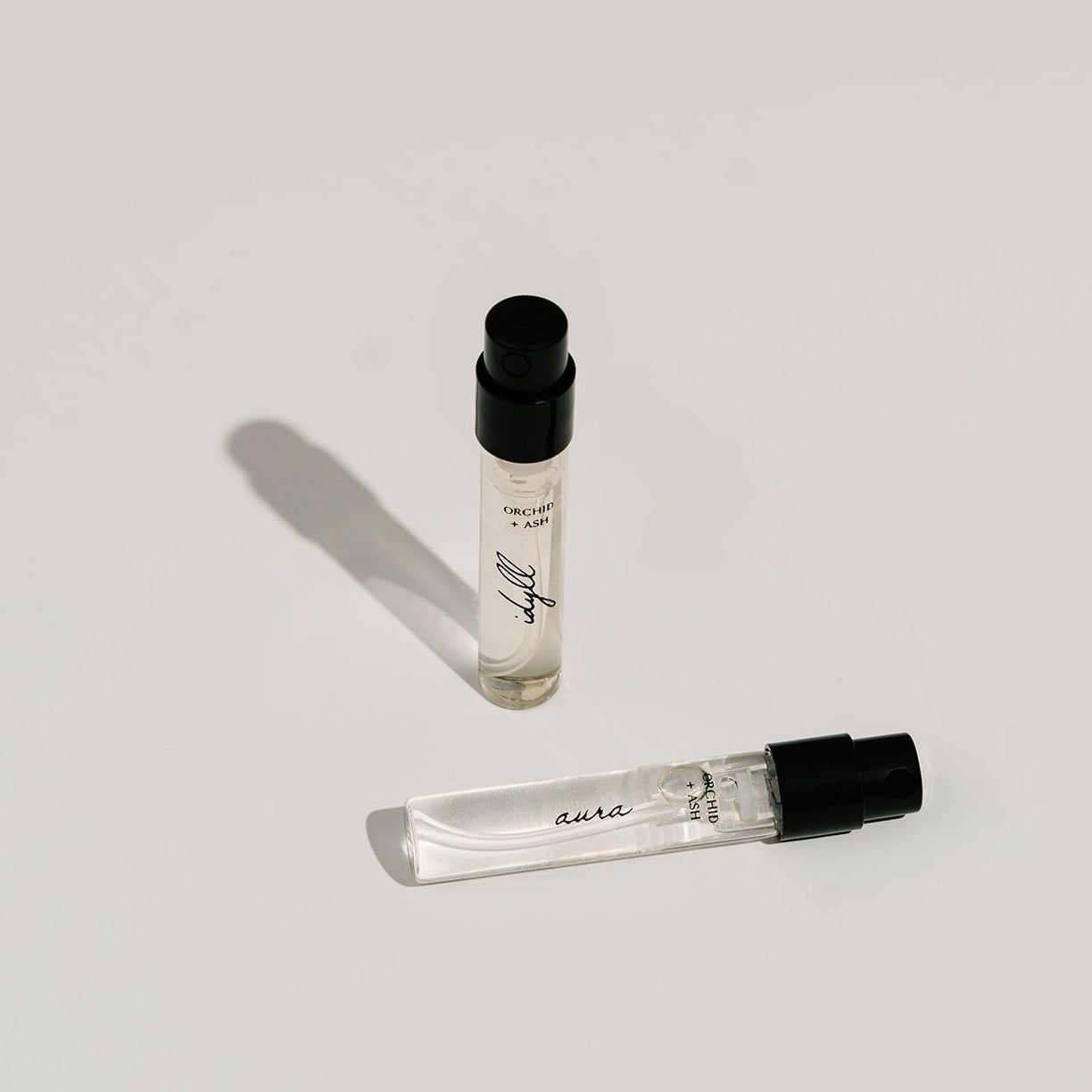 Two small perfume bottles with black caps on a light gray background