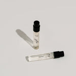 Two small perfume bottles with black caps on a light gray background