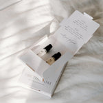 Two small bottles in an open box with a menu on a textured white surface