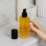 Hand holding a bottle of 'DAVDREAM' body oil on a bathroom counter.