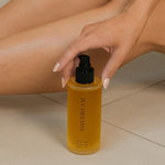 Hand holding a yellow bottle labeled 'DAYDREAM' near a person's legs on a neutral background