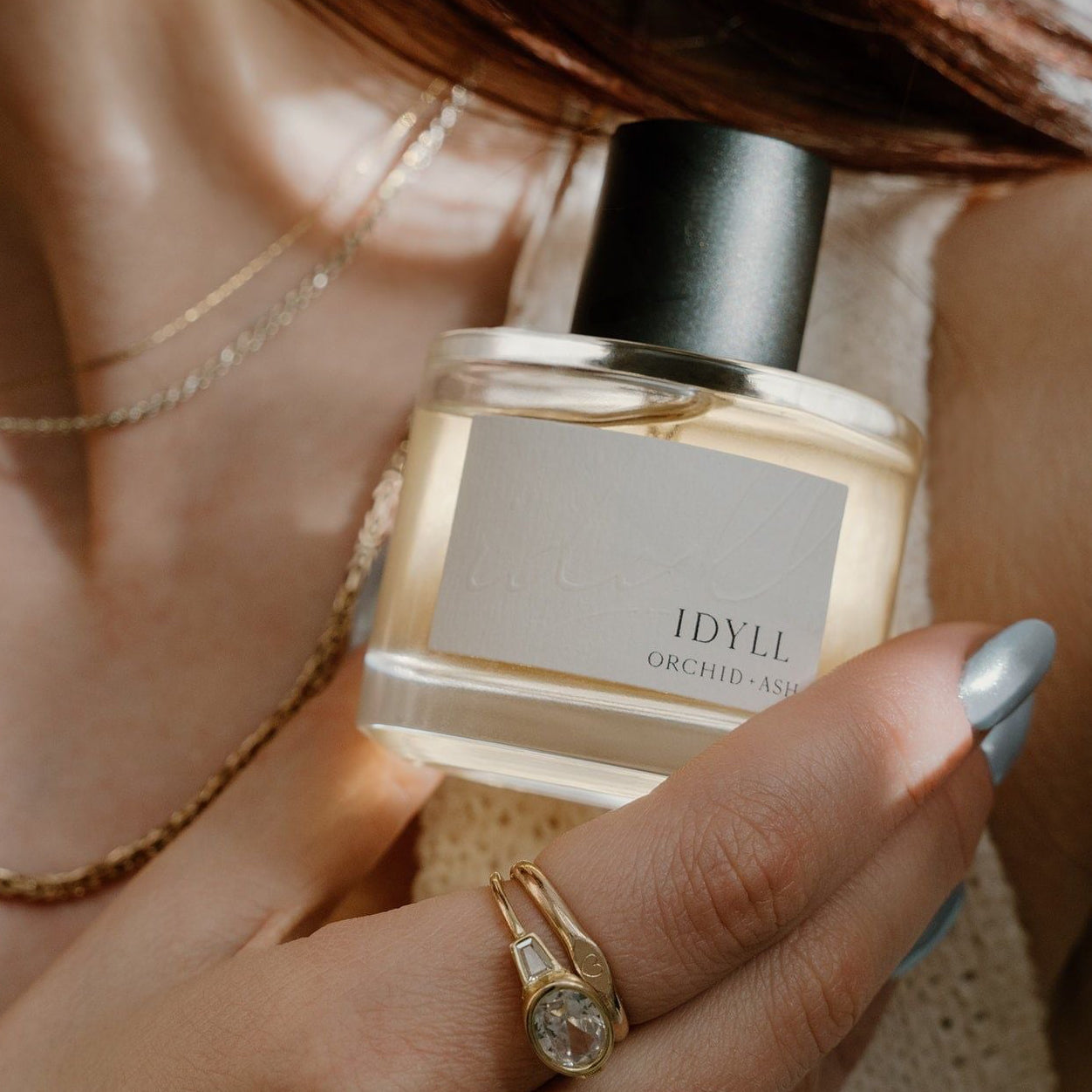 IDYLL perfume bottle held by a hand with a gold ring