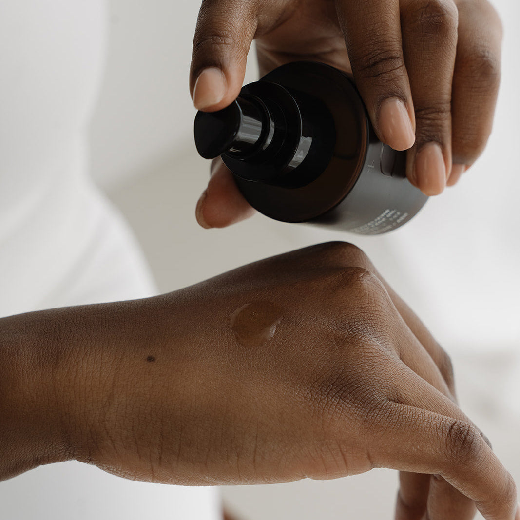 Hand applying a black bottle of skincare product to another hand on a white background