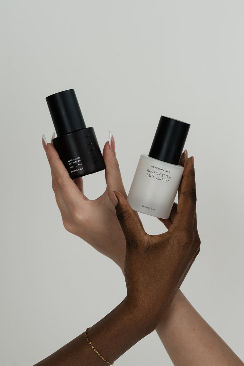 Two hands holding skincare products against a neutral background