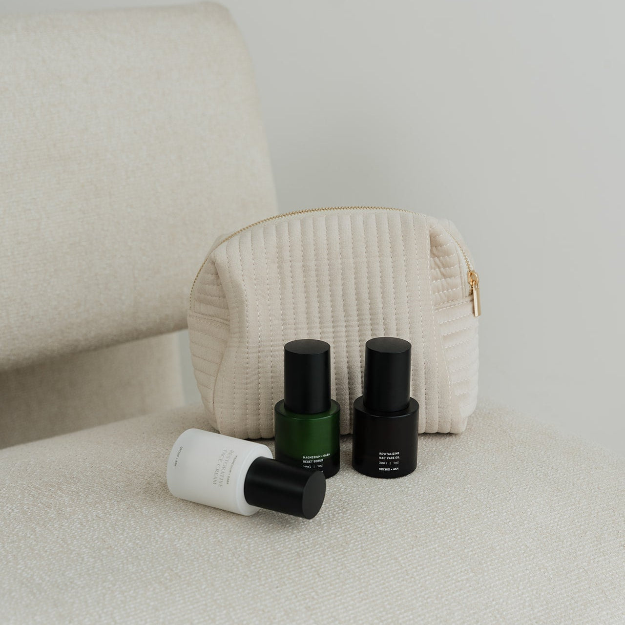 Three skincare products with black caps on a beige surface next to a textured pouch.