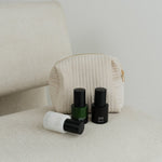 Three skincare products with black caps on a beige surface next to a textured pouch.