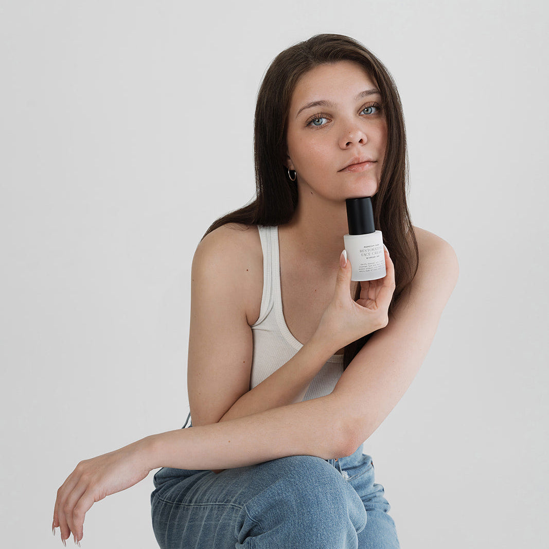 Woman holding a white bottle with a black cap against a plain background