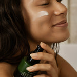 Woman applying sunscreen to her face with a bottle in a bathroom setting